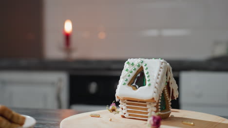 close-up of a beautifully decorated gingerbread house with icing and green beads, rotating on wooden tray, warm kitchen ambiance with blurred background