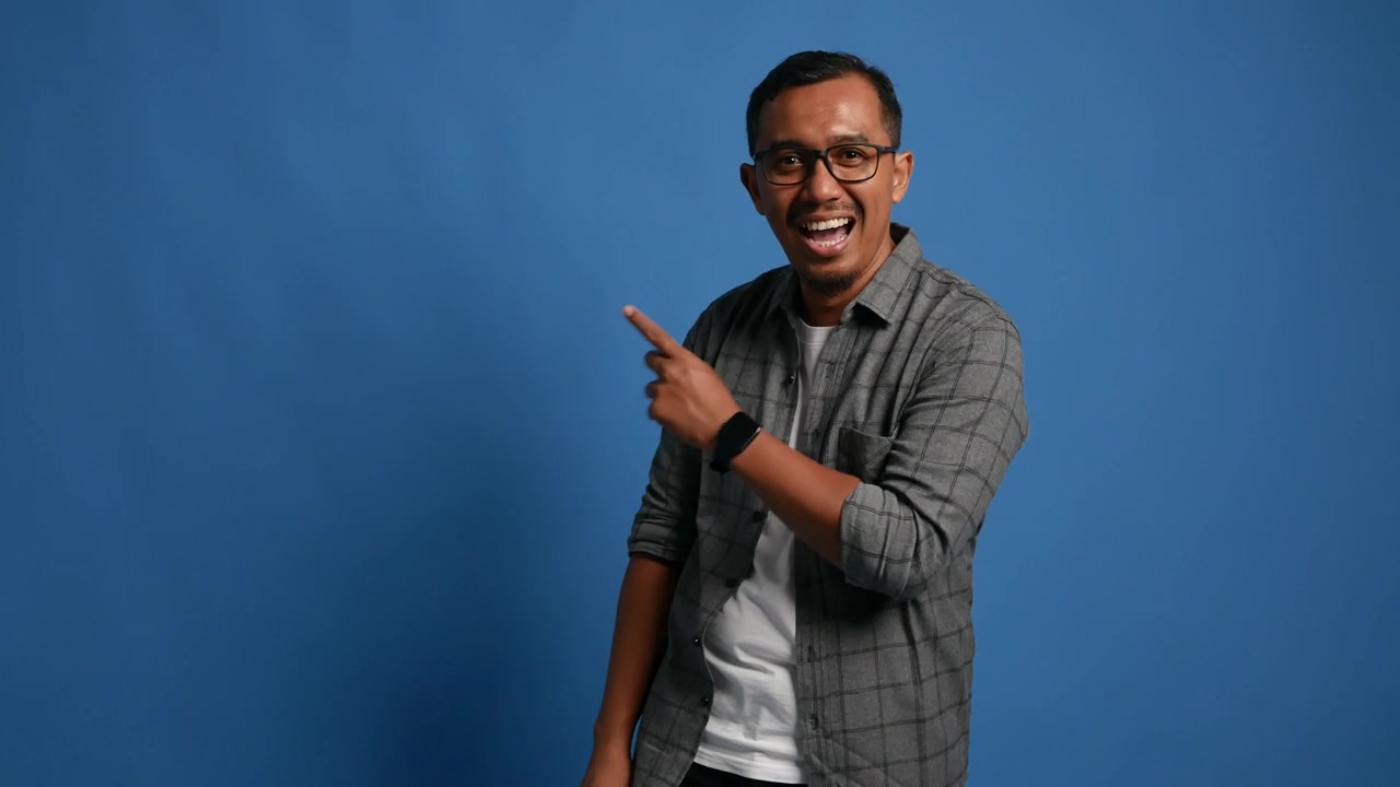 Recommending Asian adult man pointing at right side, copy space. Male presenting, showing something isolated on blue background