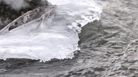 Slow-Motion-Closeup-Water-flowing-in-the-frozen-Creek,-Ice-backlit
