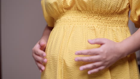 Pregnant-belly-in-a-vibrant-yellow-dress,-caressed-with-both-hands---close-up