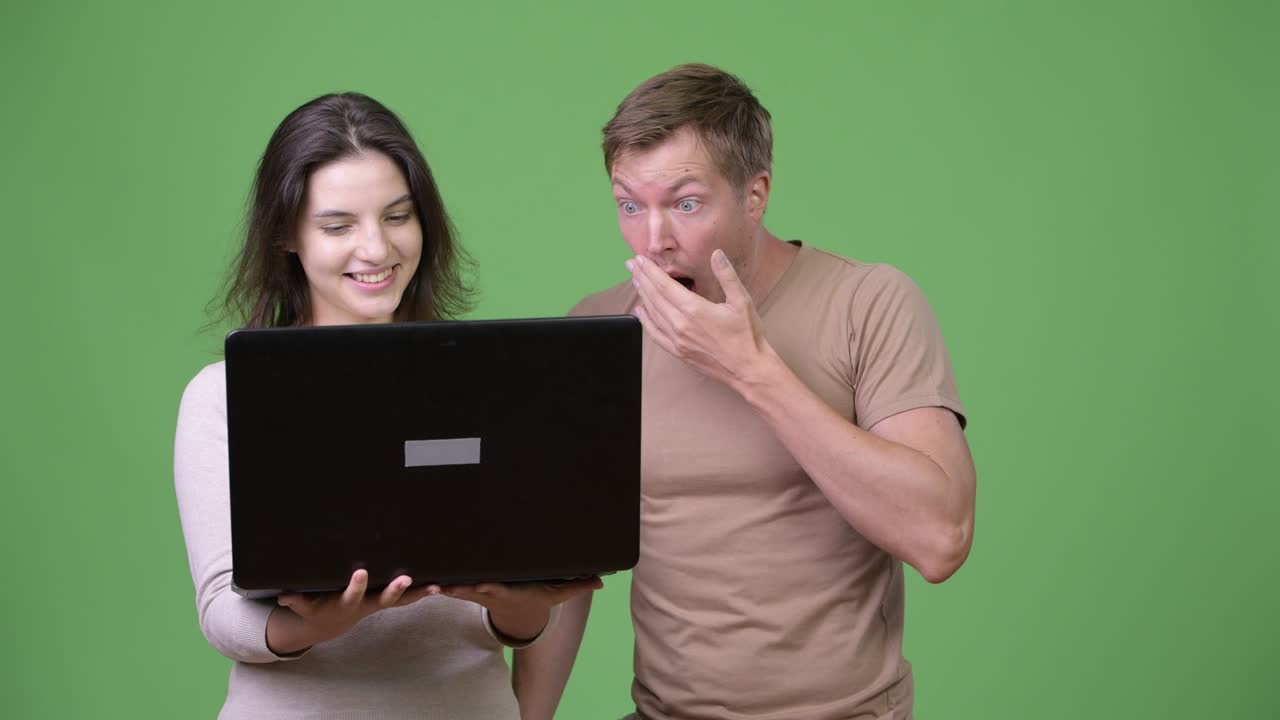 Young woman using laptop with young man looking shocked