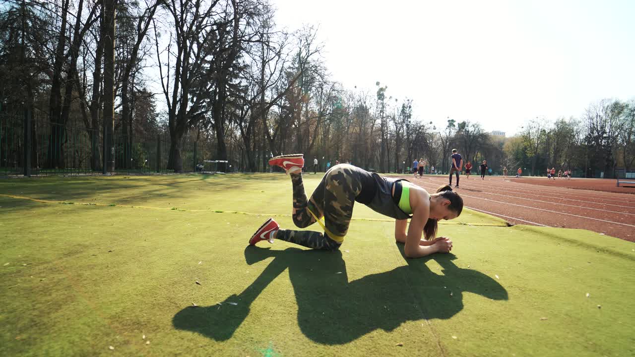 Young sporty woman runner with elastic bands outside at the stadium. Beautiful girl doing exercises. Healthy sports lifestyle