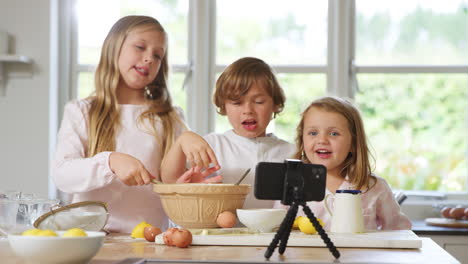 children in pyjamas baking in kitchen at home whilst vlogging on mobile phone