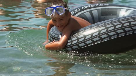 medium shot of caucasian toddler boy, enjoying the sea wearing sun mask and using an inflatable ring to swim, slow motion