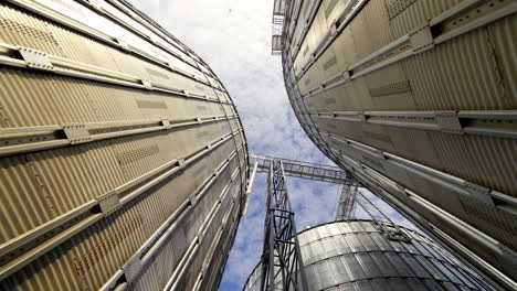 grain elevators under blue sky. huge metal grain storage tanks. silver containers. close-up. view from below.