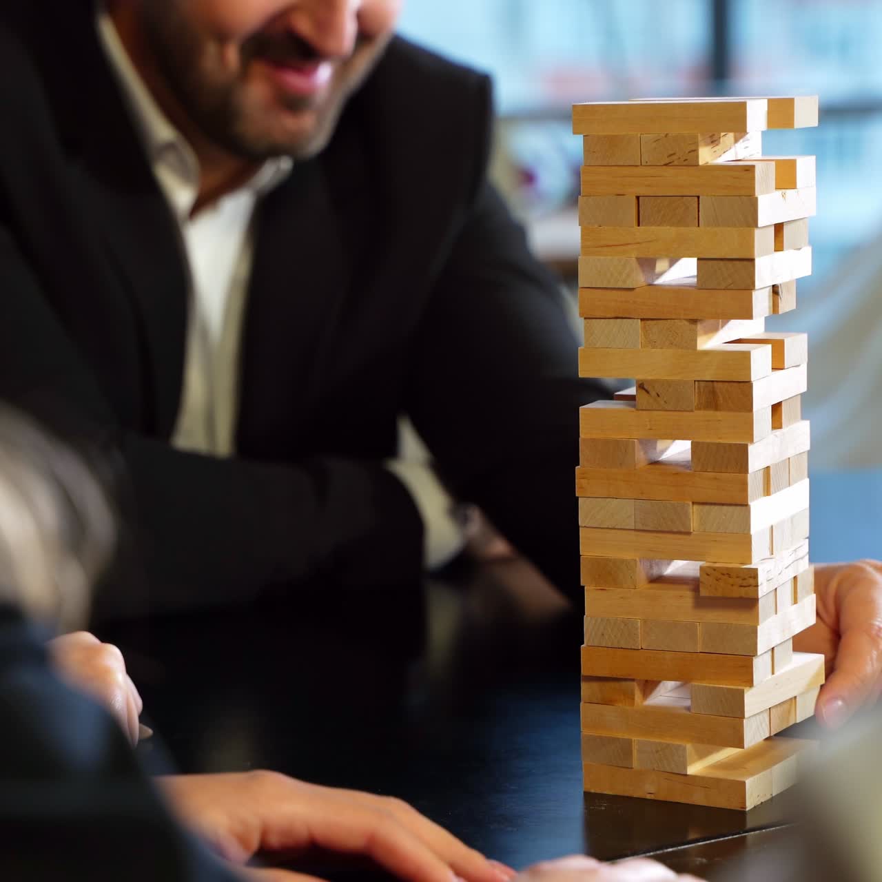 Bearded man in jacket pulls carefully jenga brick from a pile. People playing board games at leisure time