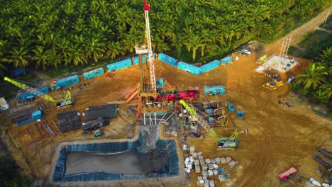 cinematic 4k drone footage of onshore drilling rig equipment structure for oil exploration and exploitation in the middle of jungle surrounded by palm oil trees during sunset and high oil price