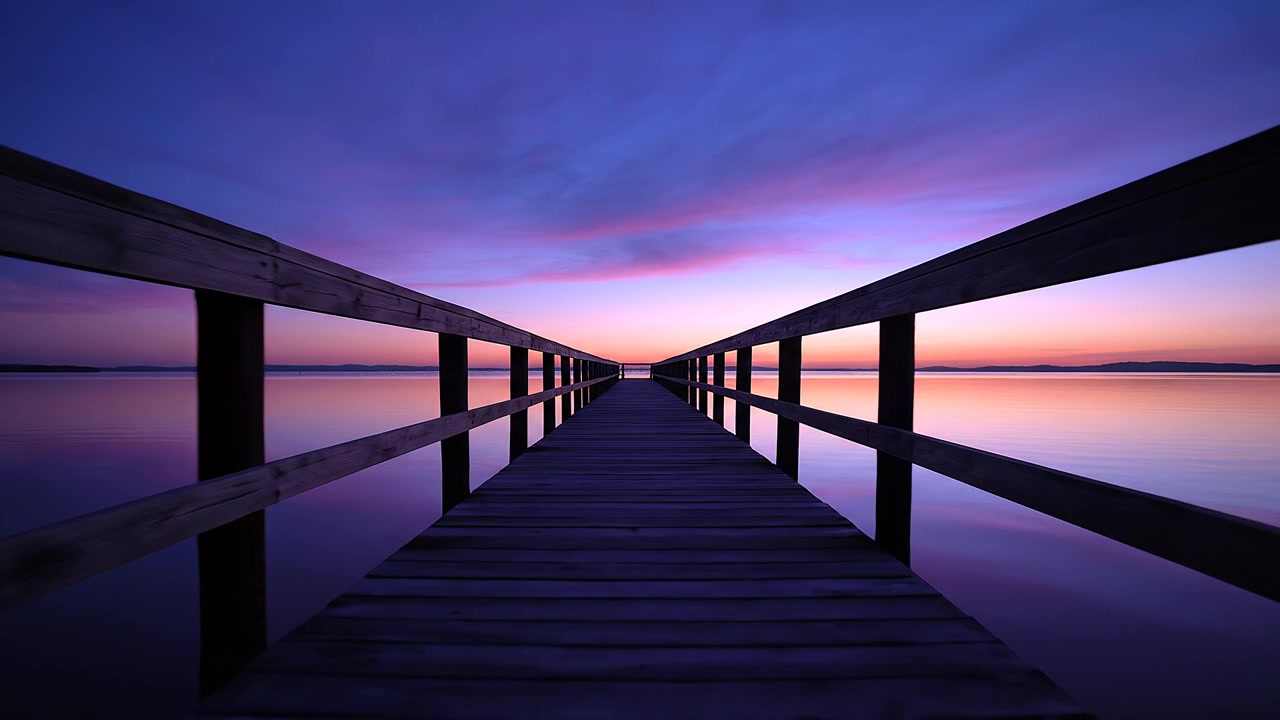 Pontile di legno che si estende in un lago calmo durante un tramonto viola vibrante.
