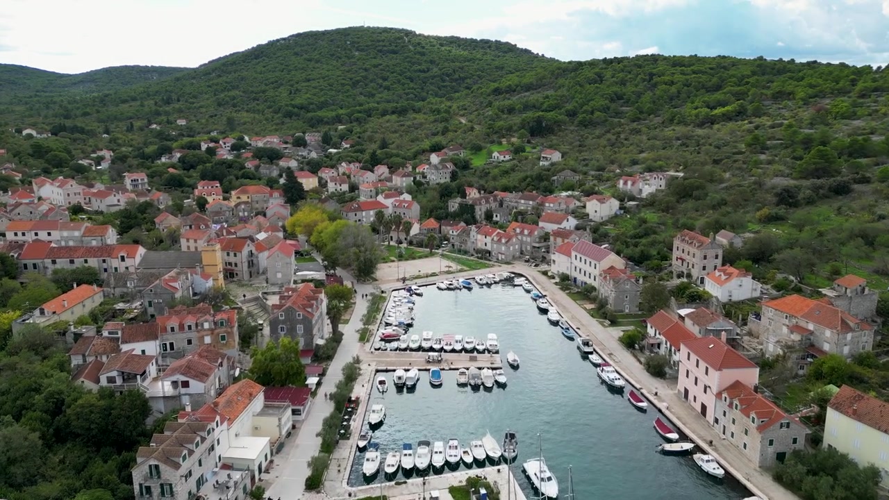 Pohyb dronu vpřed nad krásným chorvatským přístavem plným lodí na malém ostrově v Chorvatsku pod jasně modrou oblohou