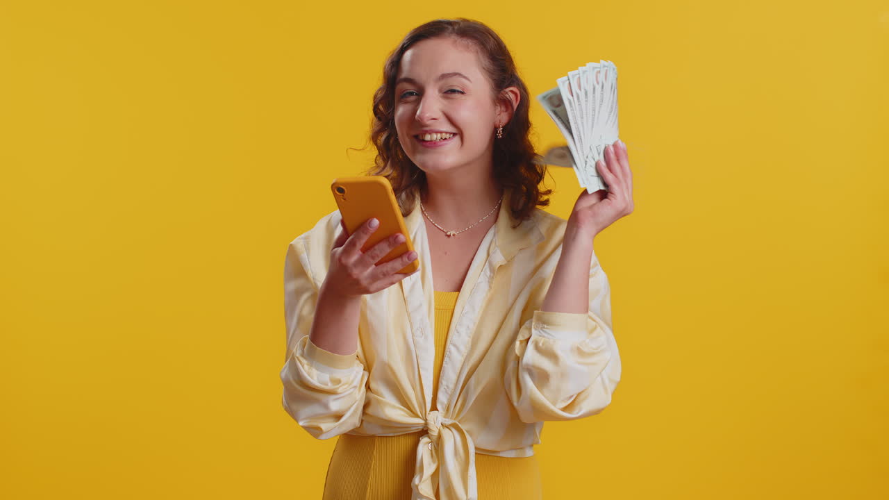 Young woman use smartphone rejoicing win receiving money dollar cash banknotes celebrating success