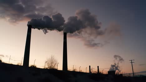 dramatic silhouette of industrial smokestacks against a colorful sunset sky, emphasizing environmental impact and industrial activity