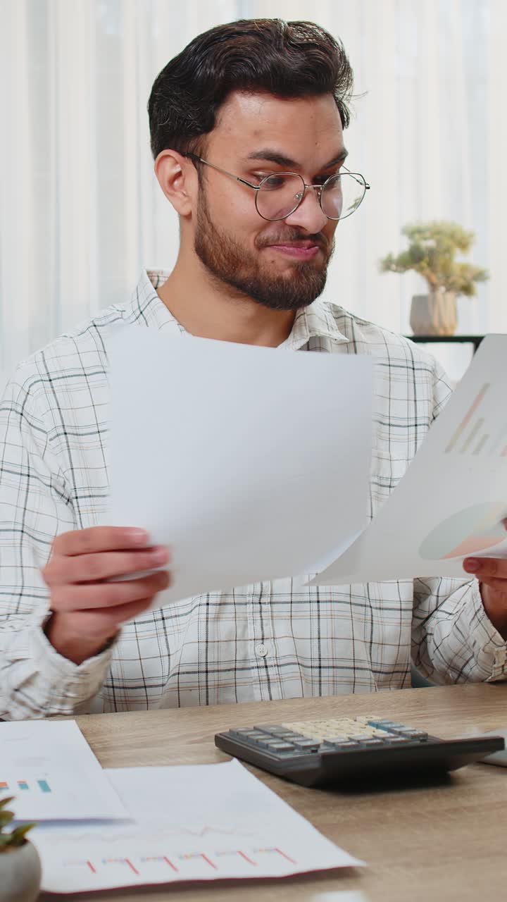 Focused indian office worker working with schedules and financial graphics while using calculator