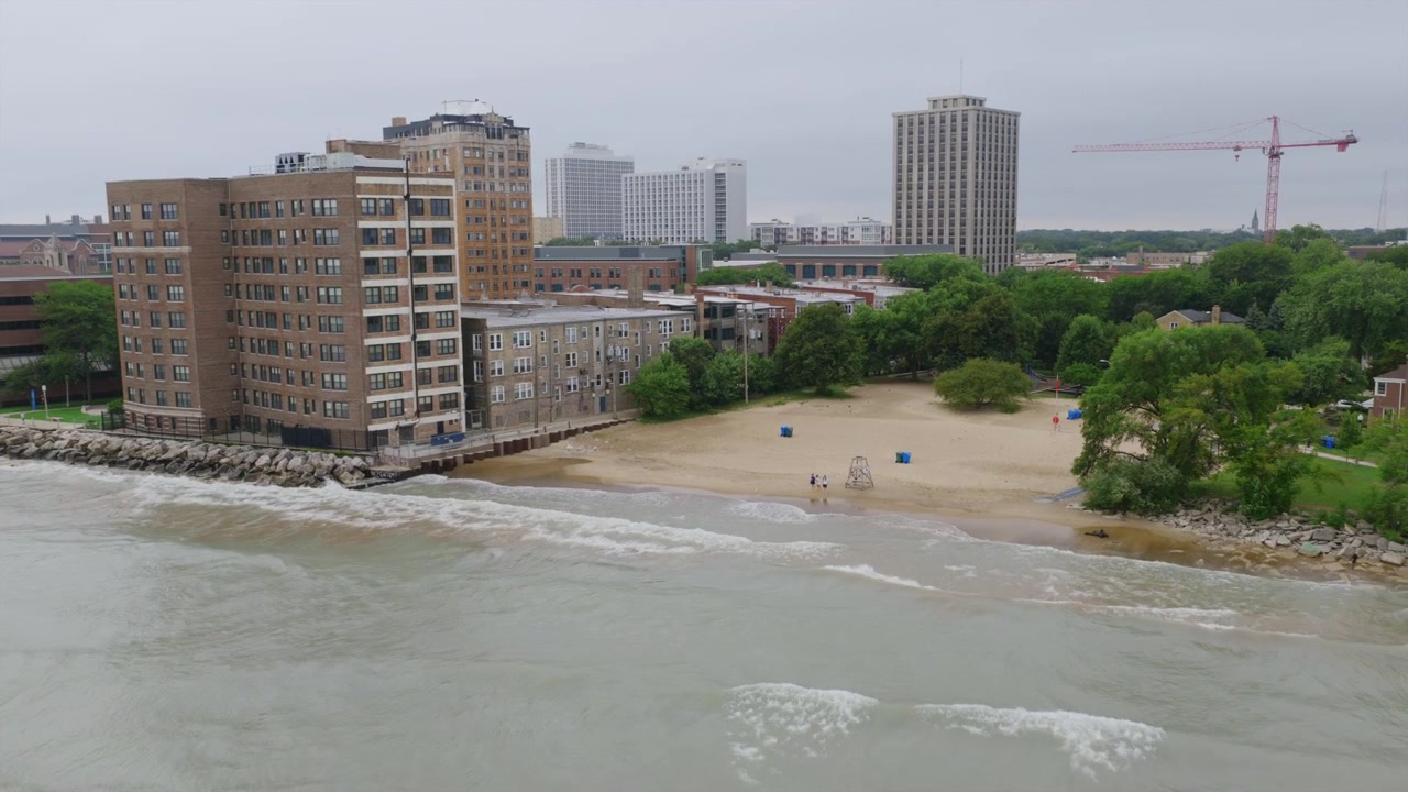 Vista aérea com drone de uma praia de Chicago junto ao Lago Michigan, emoldurada por torres de apartamentos à beira do lago e um guindaste de construção