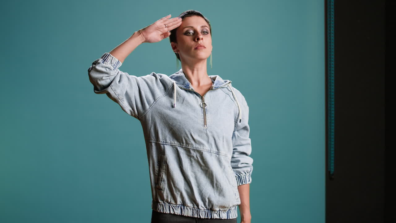 Woman in denim jacket saluting against blue background