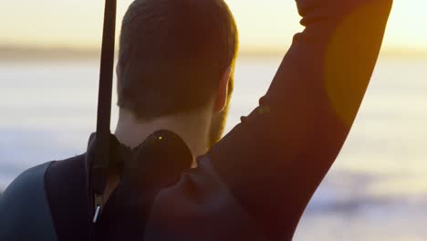 rear view of mid-adult caucasian man wearing surfing suit at the beach during sunset 4k