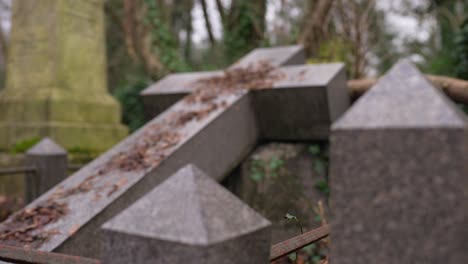 marble cross and gravestone covered in moss and brown leaves in a forest graveyard on a cloudy day