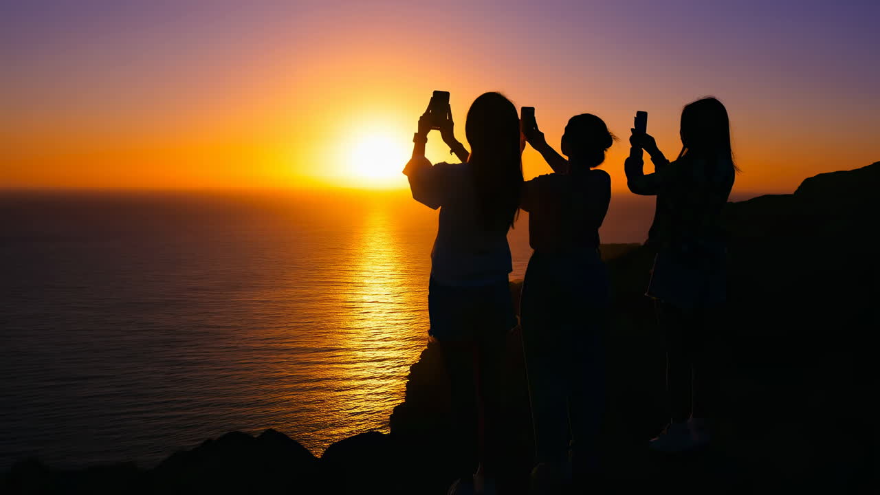 Sagome di tre donne che scattano foto di un bellissimo tramonto sull'oceano