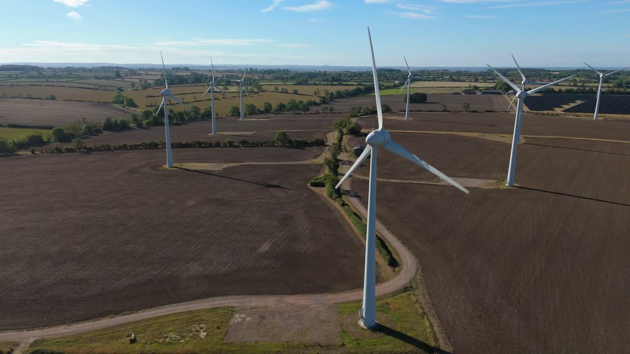 Cinematic FPV drone footage of wind turbines and solar photovoltaic farm across green countryside in England, United Kingdom