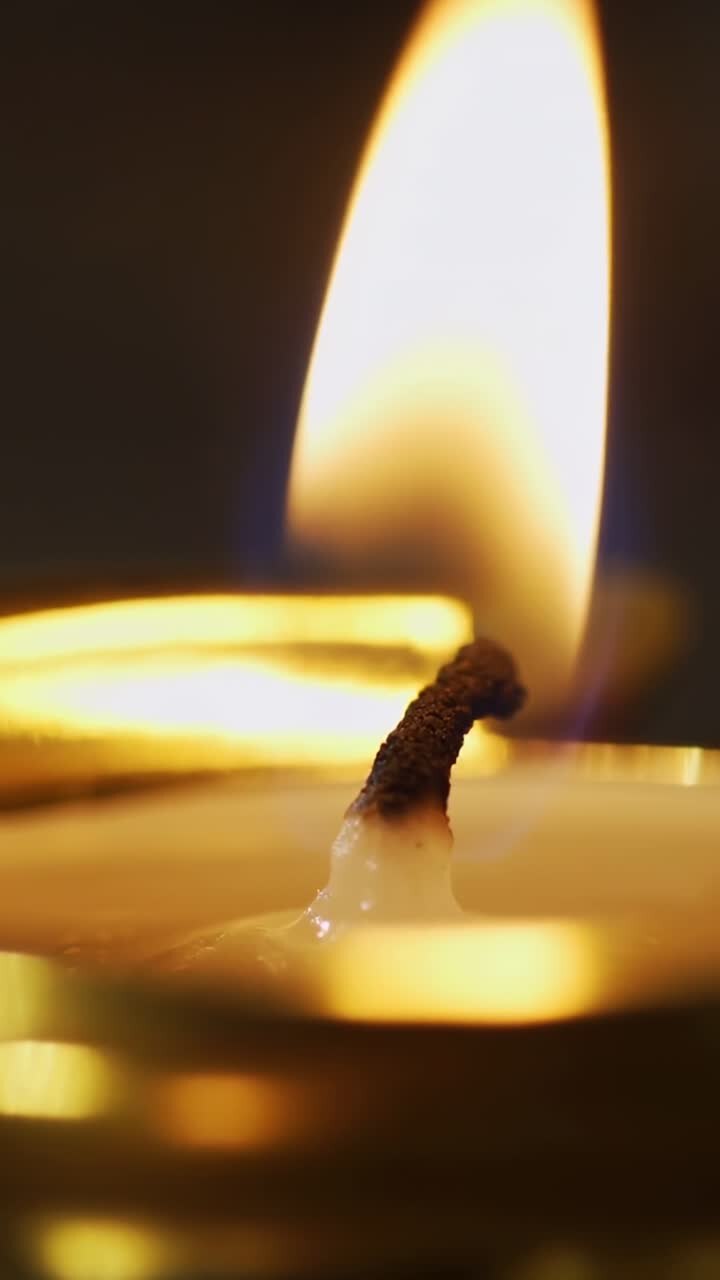 Vertical video: Wick flickering, candle flame growing to peak height over melted wax in dark room