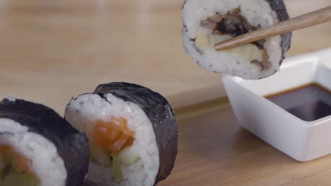 close slow motion slider shot of taking a piece of sushi from a wooden serving board with chopsticks and dipping into soy sauce