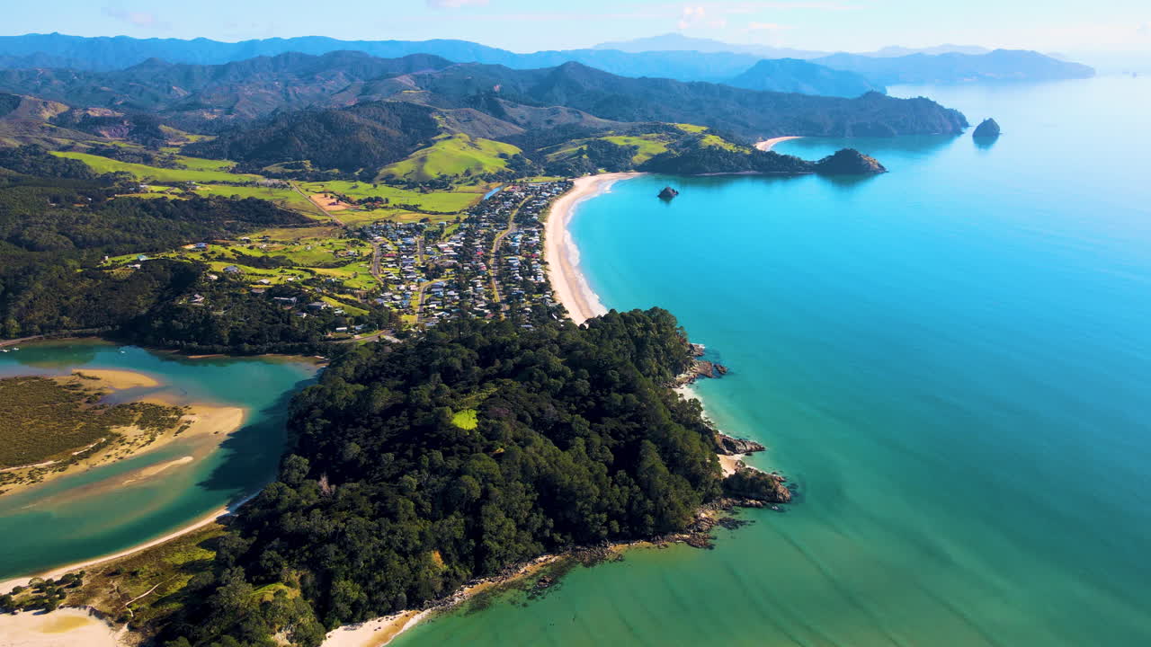 elevación aérea de la península de coromandel costera, pequeño pueblo al lado de la playa, día soleado en nueva zelanda