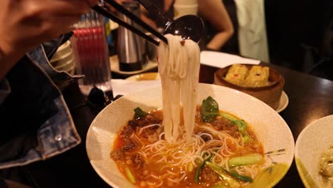 person enjoying chinese noodle soup with chopsticks