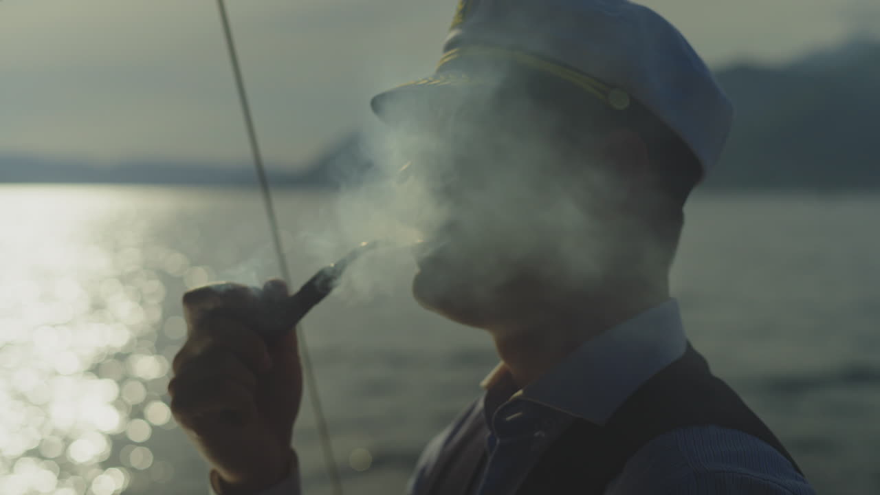 капитан курит трубку на лодке на закате