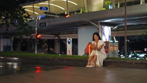 woman sitting on the sidewalk at night in a city