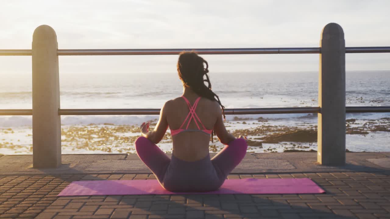 Afroamerikkalainen nainen urheiluasussa meditoimassa rantapromenadilla meren äärellä