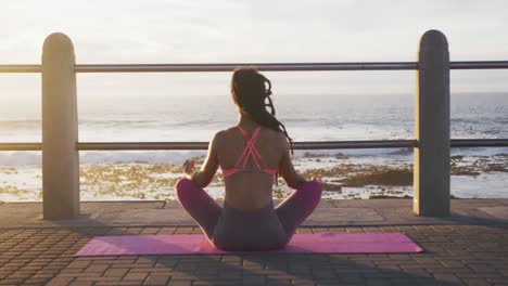 African-american-woman-in-sportswear-meditating-on-promenade-by-the-sea