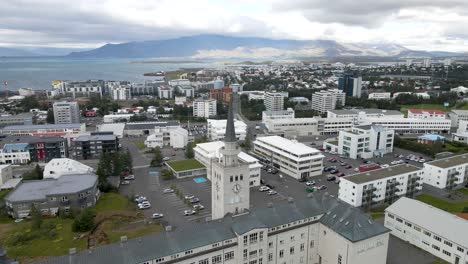 Eine-4K-Drohne-Gleitet-über-Das-Herz-Von-Reykjavik,-Während-Der-Große-Glockenturm-Als-Wache-Vor-Der-Ruhigen-Uferpromenade-Steht