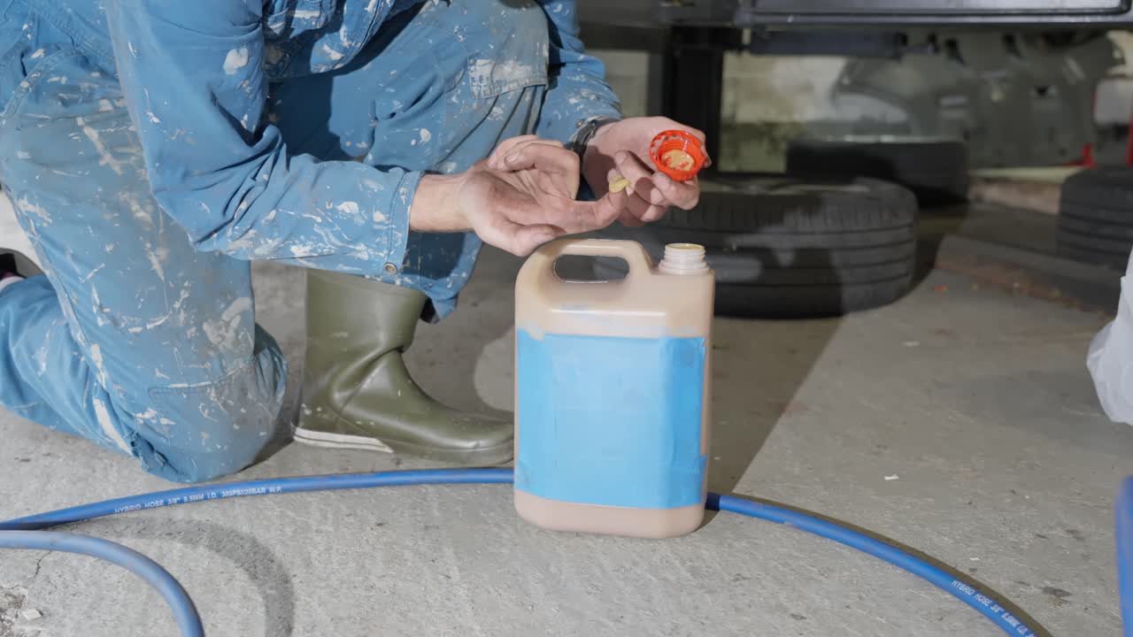 Man in workshop coveralls opens bottle of lanolin undercoating rust treatment and wipes finger to show non toxic formula