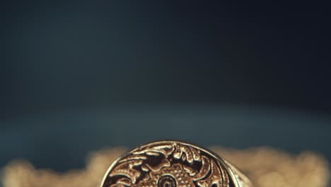 a macro detailed shot of a golden textured freemasons ring, on a mirror reflection stand, illuminati symbol, studio light, 4k video, tilt down movement, necklace shallow depth of field. cabal