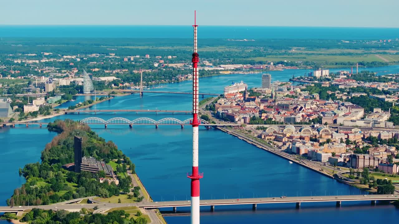 Tall TV tower stands above Daugava River with Riga skyline on bright summer day