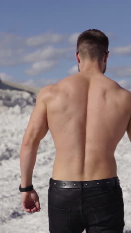athlete in bright sunny day on white canyon. backside view of sporty man in nature. shirtless bodybuilder walks in the mountains to the black car. slow motion. vertical video