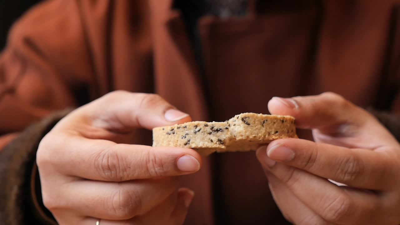 Close-Up of Hands Breaking and Eating a Seeded Cookie