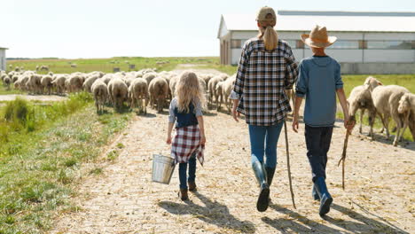 rear view of caucasian mother farmer walking with her son and daughter while the sheep flock is grazing