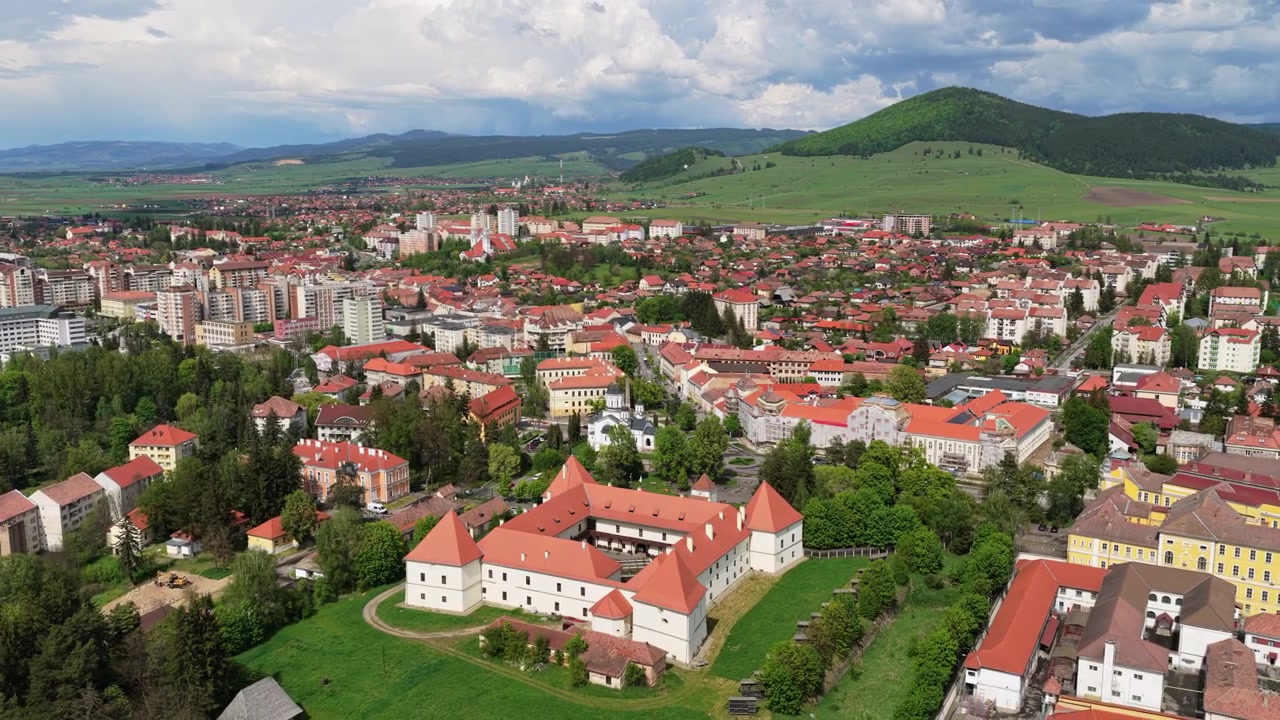 Vista aerea con drone di una città con tetti rossi e un castello, circondata da colline boscose, Harghita, Transilvania, Romania
