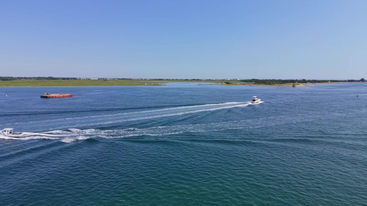 Motoscafi e chiatta che navigano lungo un canale blu dell'estuario a Salisbury, Massachusetts. Volo aereo basso in avanti.