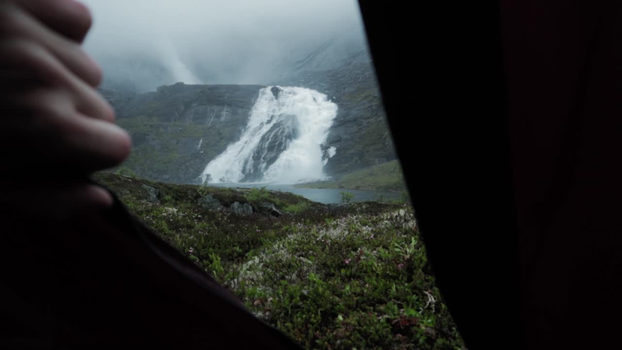 Person hand reveal Husedalen waterfall in Norway, view from tent