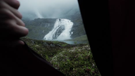 person hand reveal husedalen waterfall in norway, view from tent