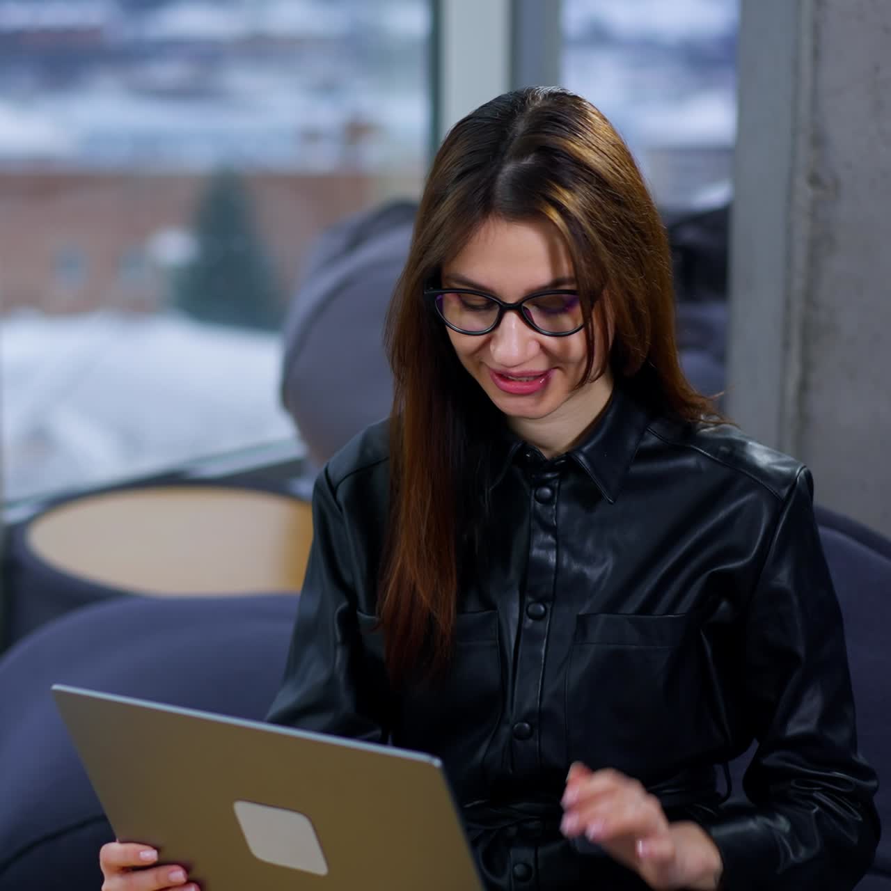 Brunette woman in glasses typing on the keyboard of laptop. Lady is surprised or excited from message or news. Blurred backdrop