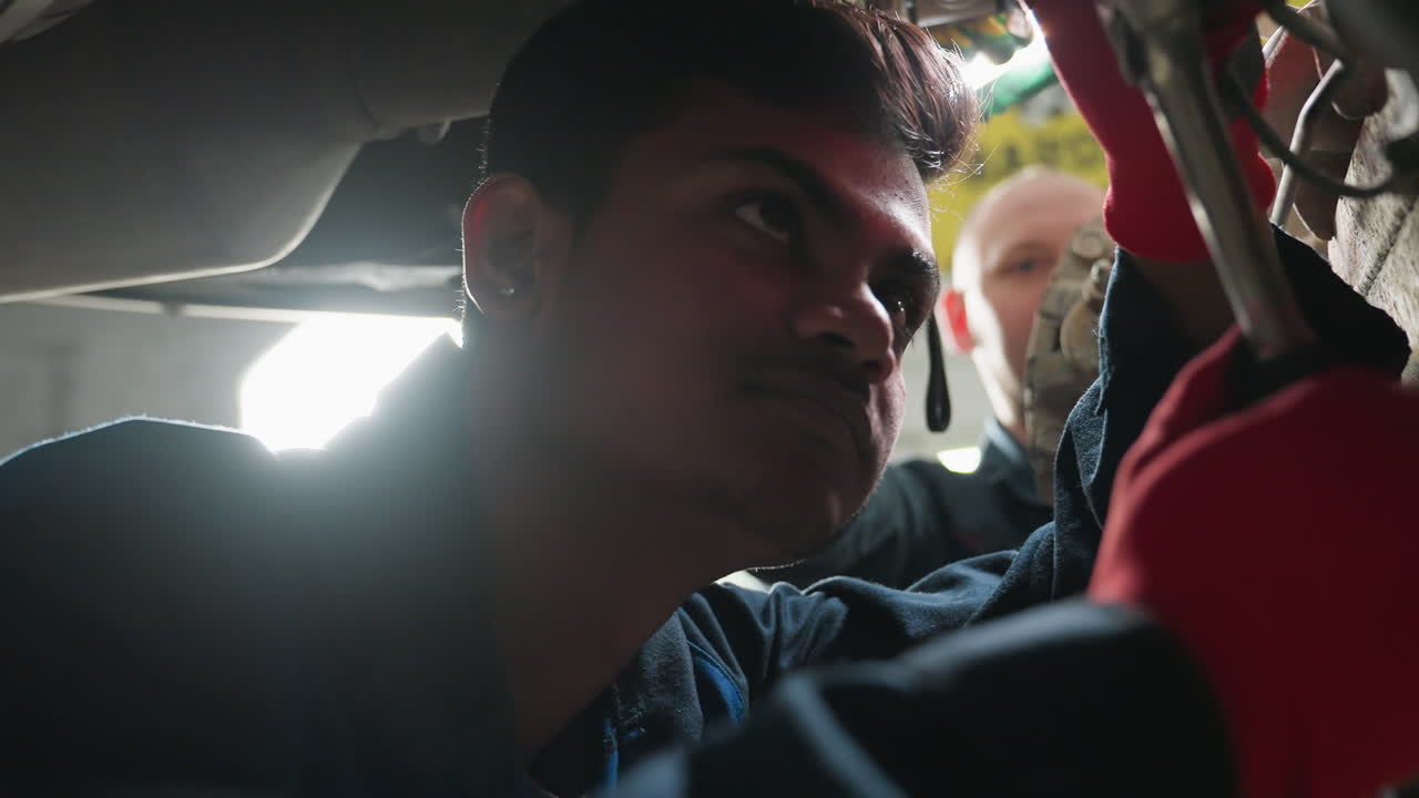 자동차 수리 작업에 종사하는 엔지니어, 실험실 기술자가 태블릿을 가지고 접근하여 관찰하고 메모를 취하는 동안, 도구와 함께 기계 작업실 설정, 승강된 차량, 진행 중인 기술 검사