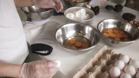 baker's hands cracking eggs into stainless mixing bowl