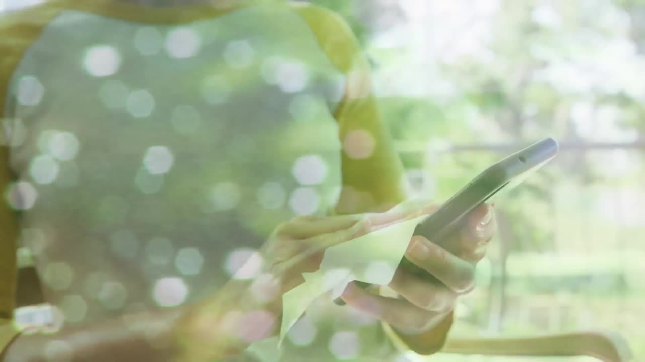 animación de puntos de luz sobre una mujer caucásica con máscara facial desinfectando un teléfono inteligente