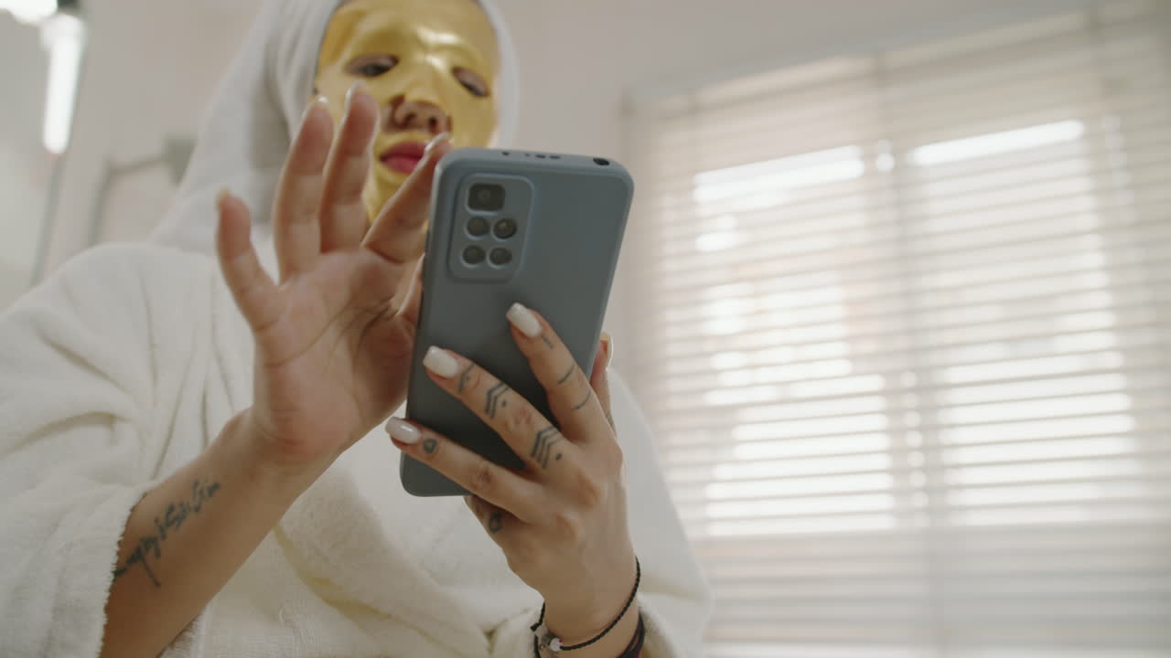 Woman Using Phone while Wearing Golden Sheet Mask on Face
