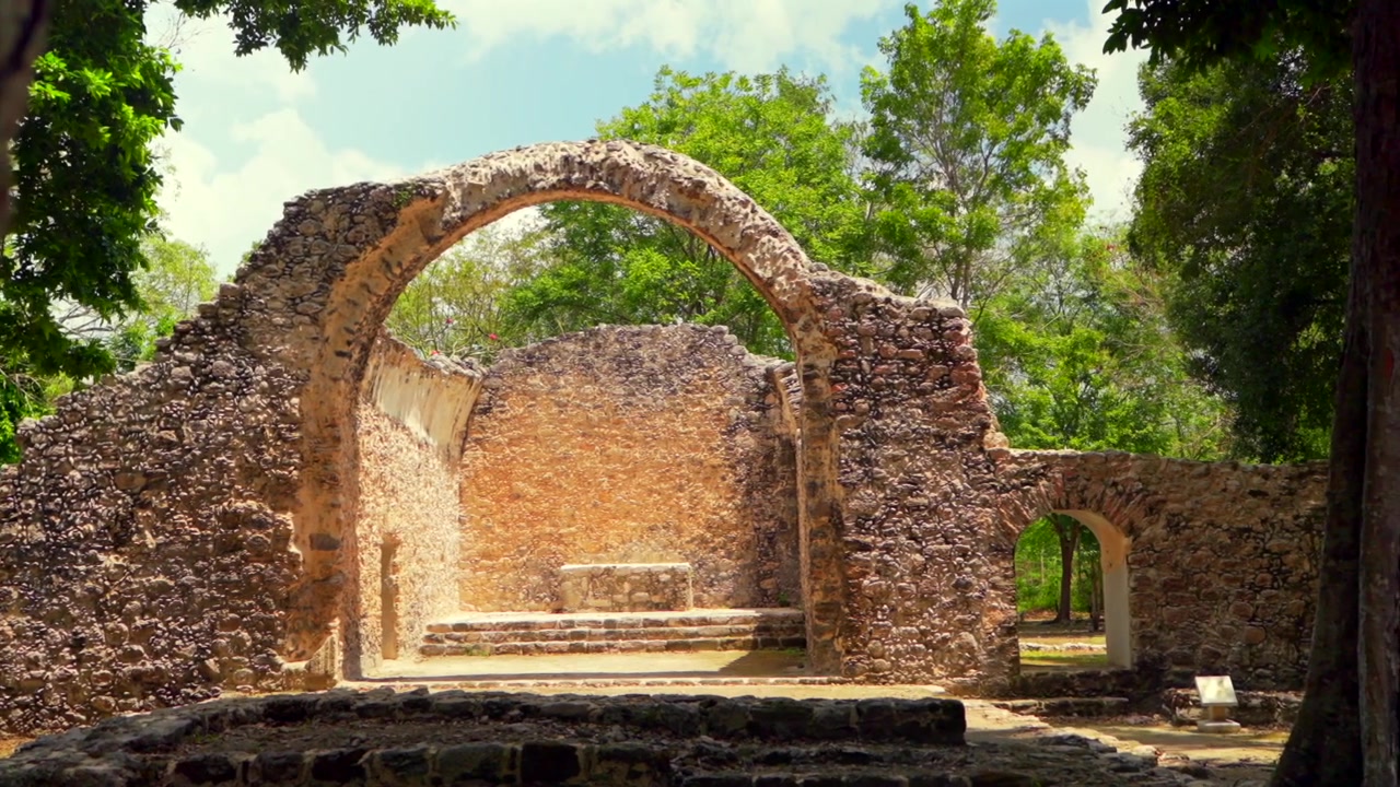 Ripresa panoramica fluida che rivela le antiche rovine della Cappella Spagnola del XVI secolo a Oxtankah, un importante sito archeologico Maya in Quintana Roo, Messico, circondato da alberi verdi e lussureggianti