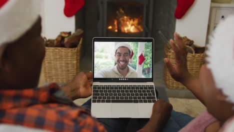pareja afroamericana con sombreros de santa usando una computadora portátil para una videollamada de navidad con un hombre en la pantalla