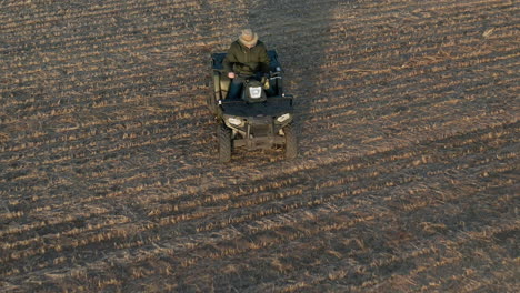 man driving atv in farm field and taking a soli sample, aerial follow