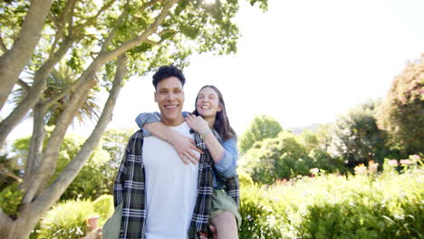 happy diverse couple playing piggyback and walking in sunny garden, copy space, in slow motion